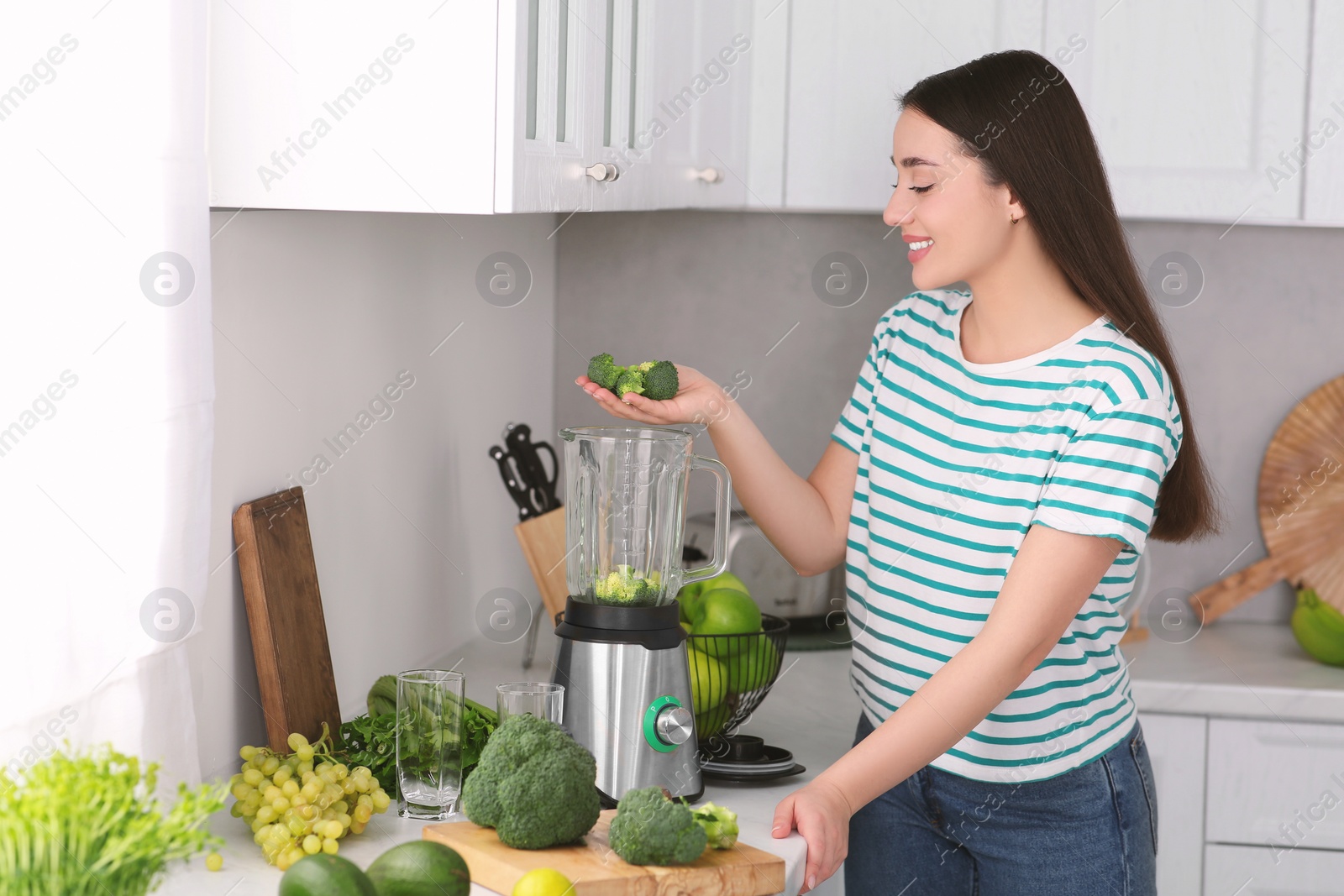 Photo of Woman adding broccoli into blender for smoothie in kitchen
