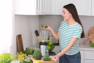 Woman adding broccoli into blender for smoothie in kitchen