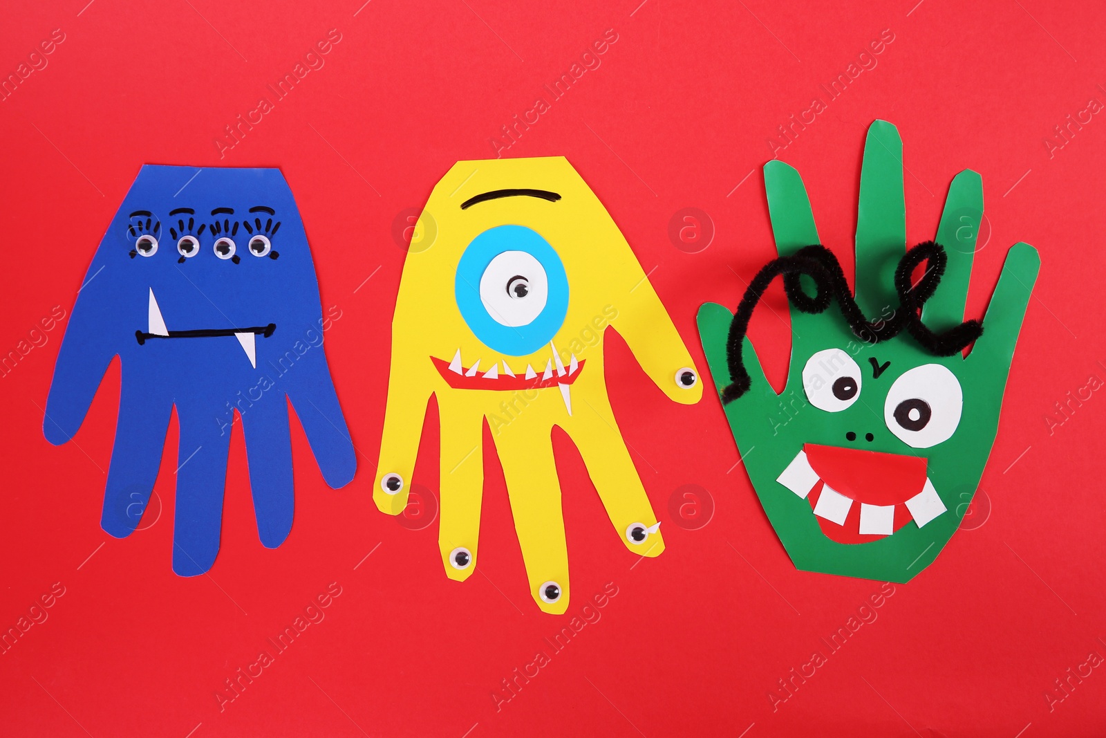 Photo of Funny hand shaped monsters on red background, flat lay. Halloween decoration