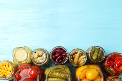 Glass jars with different pickled vegetables on light blue wooden table, flat lay. Space for text