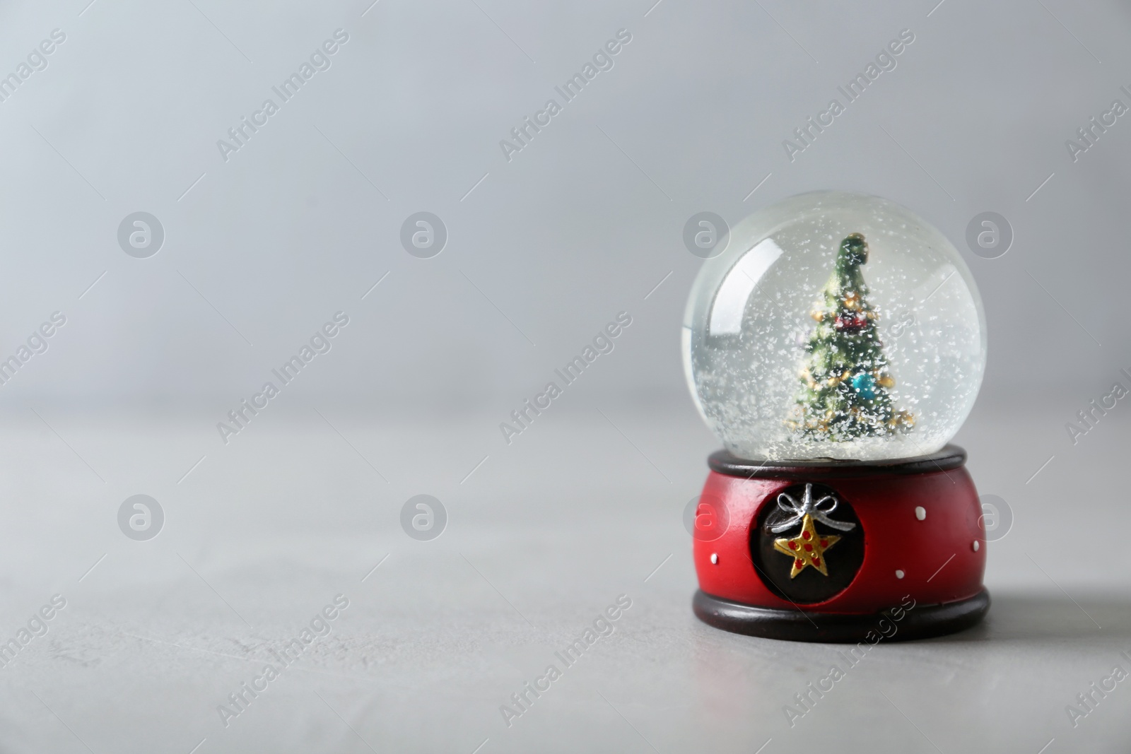 Photo of Snow globe with Christmas tree on grey table, space for text