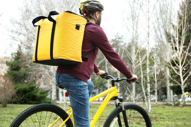 Courier with thermo bag riding bicycle outdoors. Food delivery service