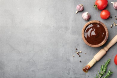 Flat lay composition with tasty barbeque sauce in bowl on grey textured table. Space for text