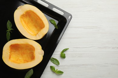 Photo of Sheet pan with raw spaghetti squash halves and basil on white wooden table, flat lay. Space for text