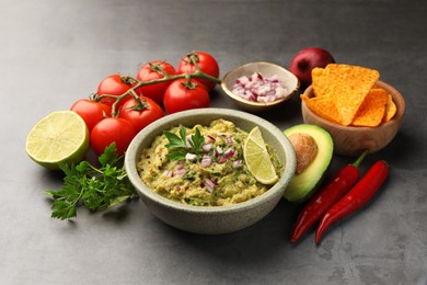 Photo of Bowl of delicious guacamole, nachos chips and ingredients on grey table