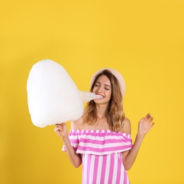 Photo of Happy young woman eating cotton candy on yellow background