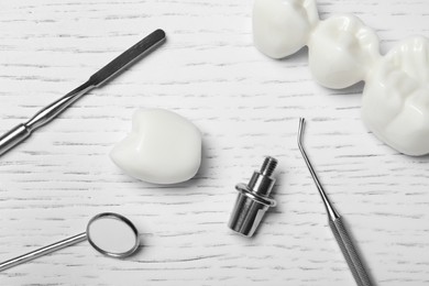 Abutment, crown of dental implant near bridge and medical tools on white wooden table, flat lay