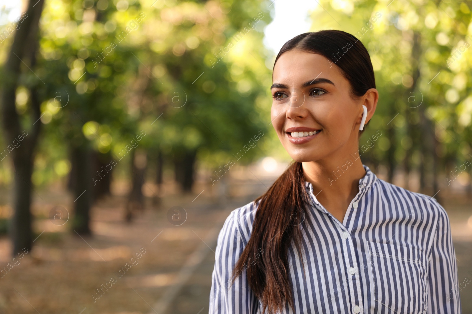 Photo of Young woman with wireless earphones in park