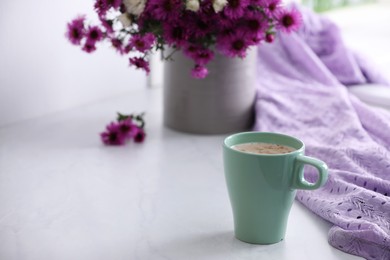 Photo of Cup of aromatic coffee, beautiful flowers and violet cloth on white table, space for text