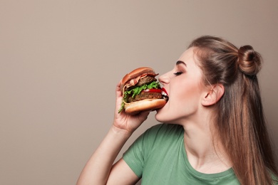 Photo of Pretty woman eating tasty burger on color background. Space for text