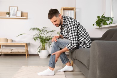 Photo of Man suffering from pain in leg on sofa at home, space for text