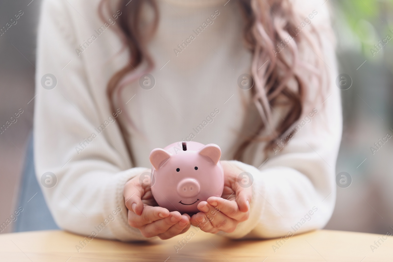 Photo of Woman holding piggy bank at table, closeup