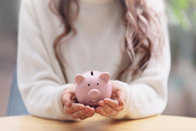 Photo of Woman holding piggy bank at table, closeup