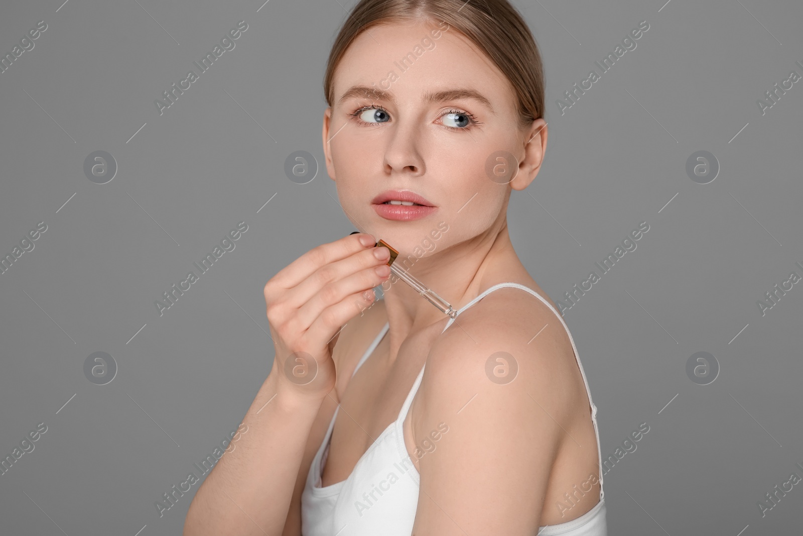 Photo of Beautiful young woman applying essential oil onto shoulder on grey background