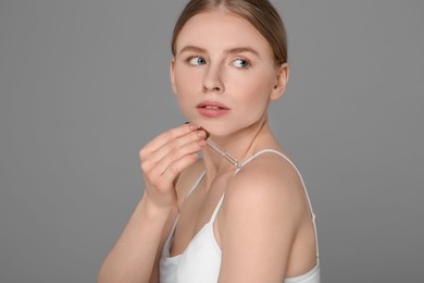 Beautiful young woman applying essential oil onto shoulder on grey background