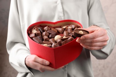 Photo of Woman holding heart shaped box with delicious chocolate candies, closeup