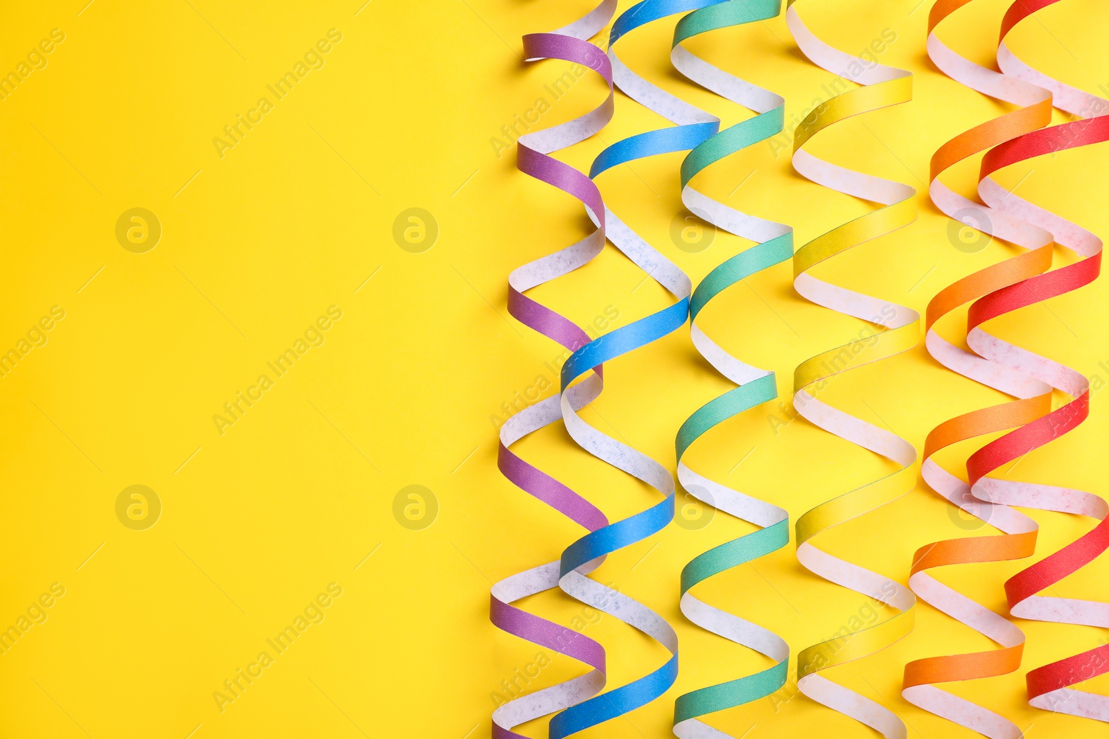 Photo of Rainbow serpentine streamers on yellow background, flat lay with space for text. LGBT pride