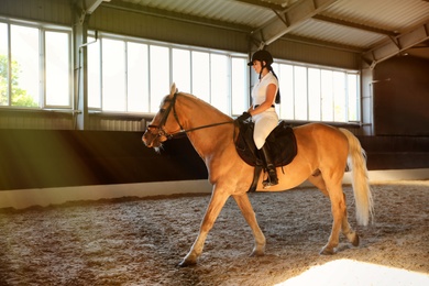 Photo of Young woman in equestrian suit riding horse indoors. Beautiful pet