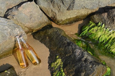 Photo of Bottles of cold beer near rocks on sandy beach, space for text