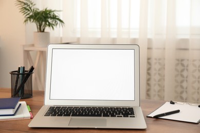 Modern laptop with blank screen on table at home