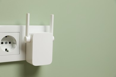 Photo of Wireless Wi-Fi repeater on light green wall, space for text