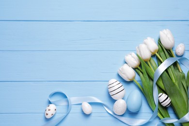 Photo of Flat lay composition of painted Easter eggs and tulip flowers on light blue wooden table. Space for text