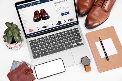 Online store website on laptop screen. Computer, smartphone, stationery, credit cards, men's shoes and accessories on white background, above view