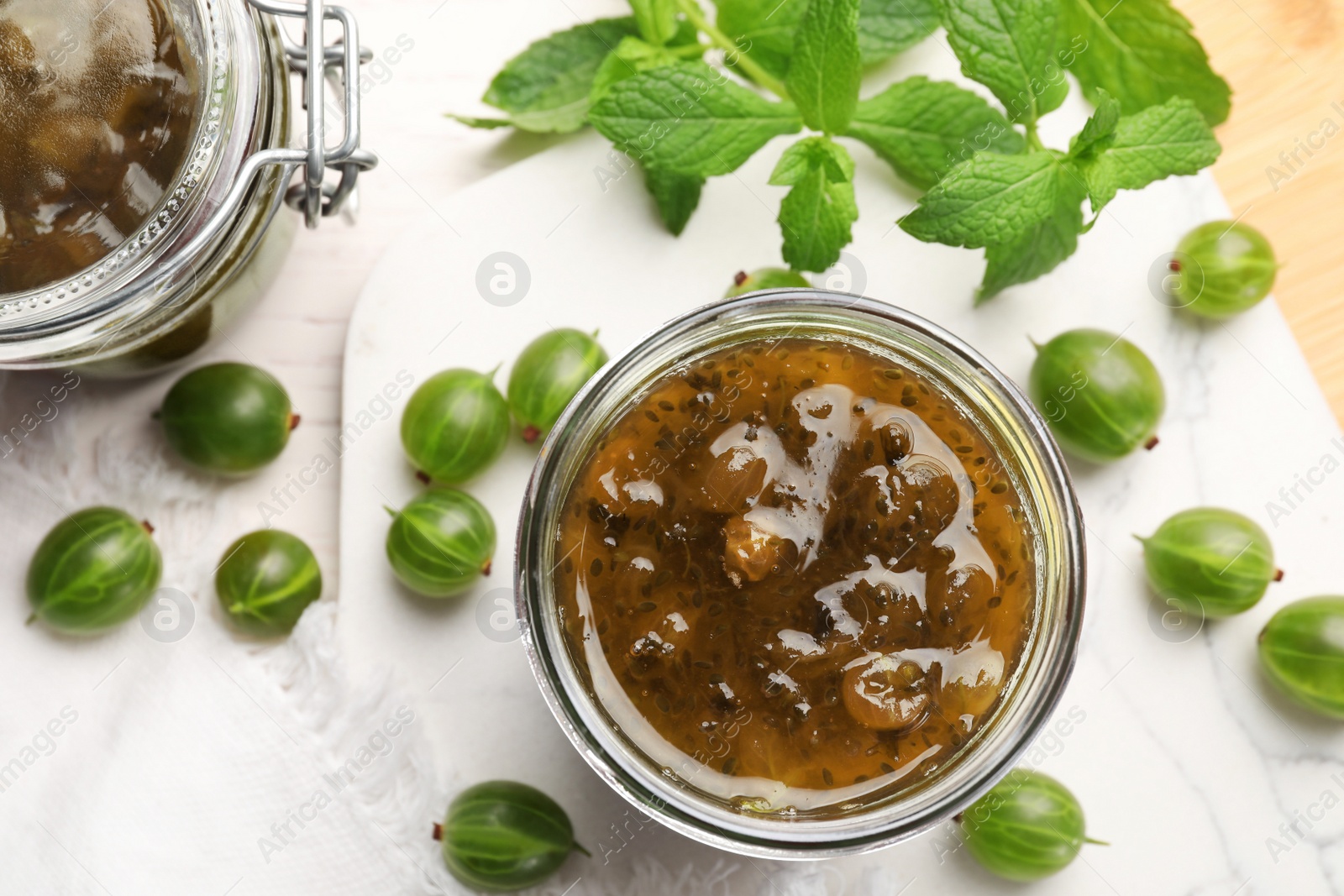 Photo of Jar of delicious gooseberry jam and fresh berries on white wooden table, flat lay