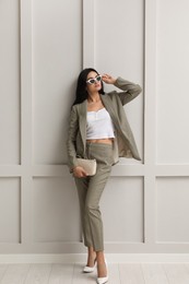 Full length portrait of beautiful woman in formal suit near light grey wall. Business attire