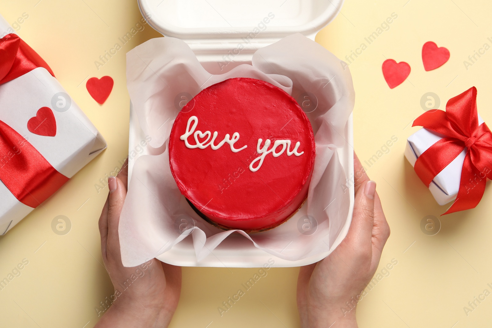 Photo of Woman holding takeaway box with bento cake at beige table, top view. St. Valentine's day surprise