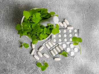 Photo of Mortar with fresh green celandine and pills on light grey table, flat lay