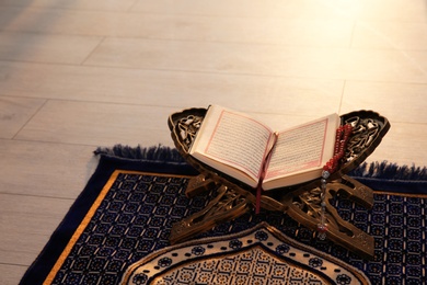 Rehal with open Quran and Muslim prayer beads on rug indoors