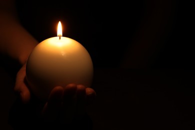 Photo of Woman holding burning candle in hand on black background, closeup. Space for text