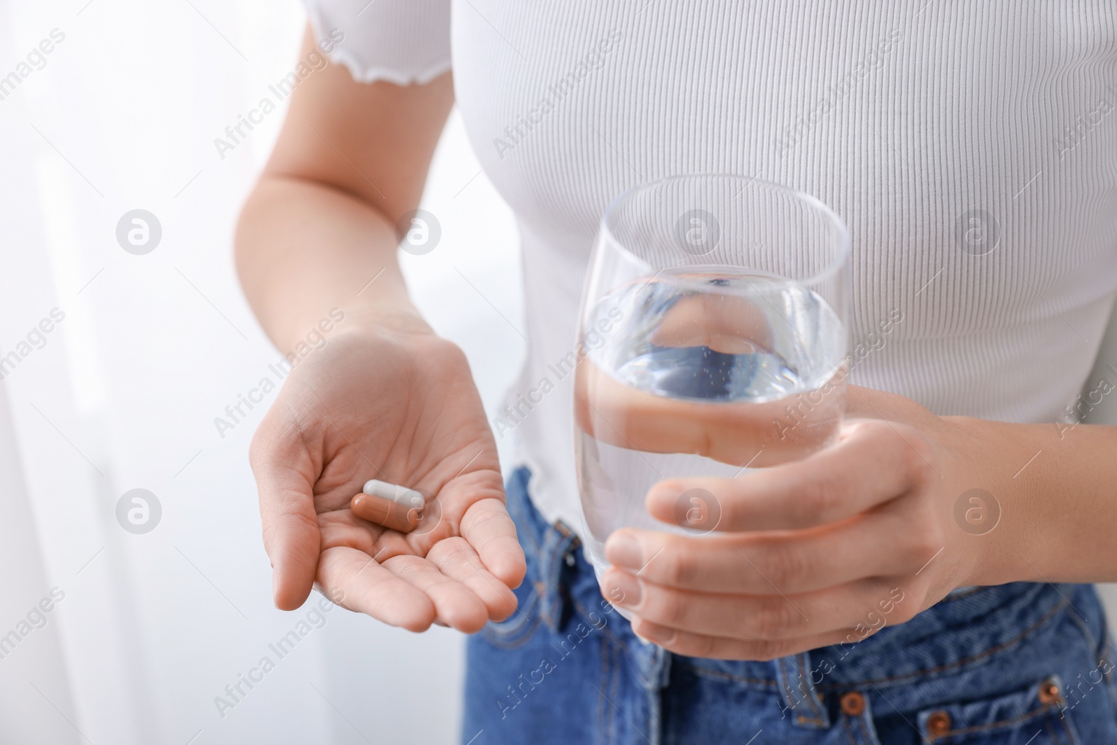 Photo of Woman with vitamin pills and glass of water indoors, closeup