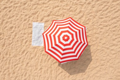 Image of Striped beach umbrella near towel on sand, aerial view