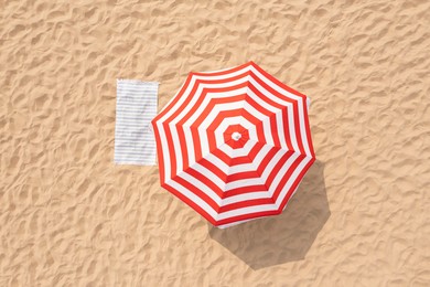 Striped beach umbrella near towel on sand, aerial view