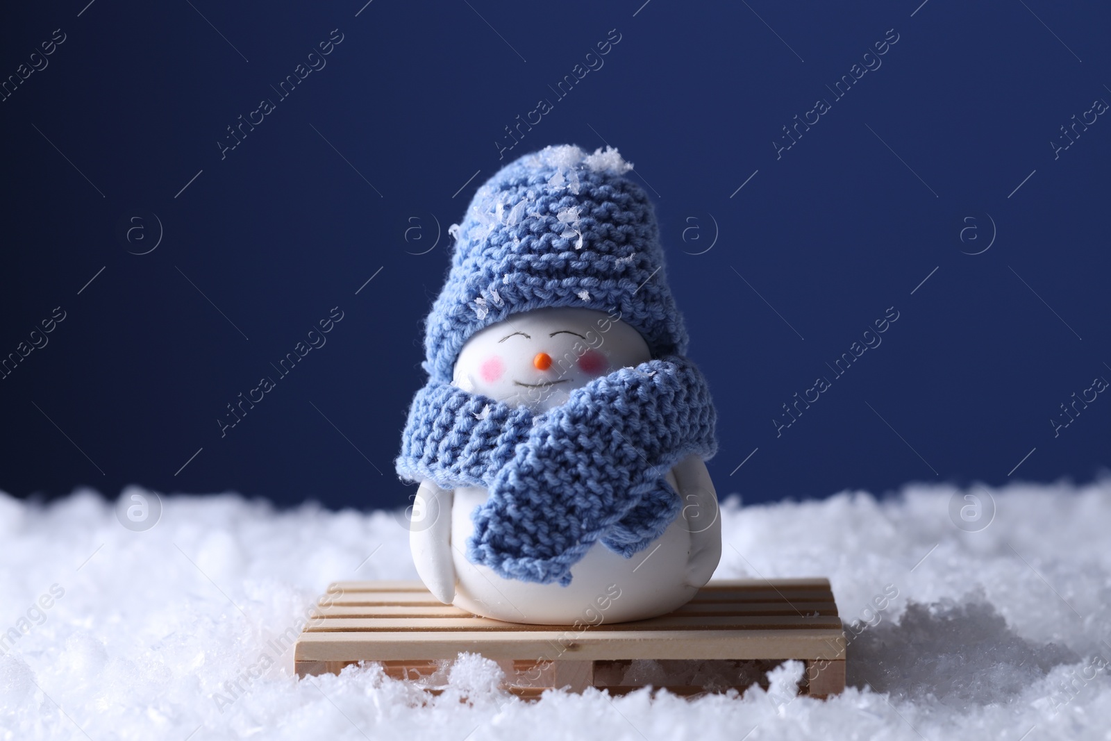 Photo of Cute decorative snowman on artificial snow against blue background, closeup