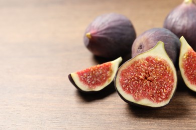 Photo of Whole and cut ripe figs on wooden table, closeup. Space for text