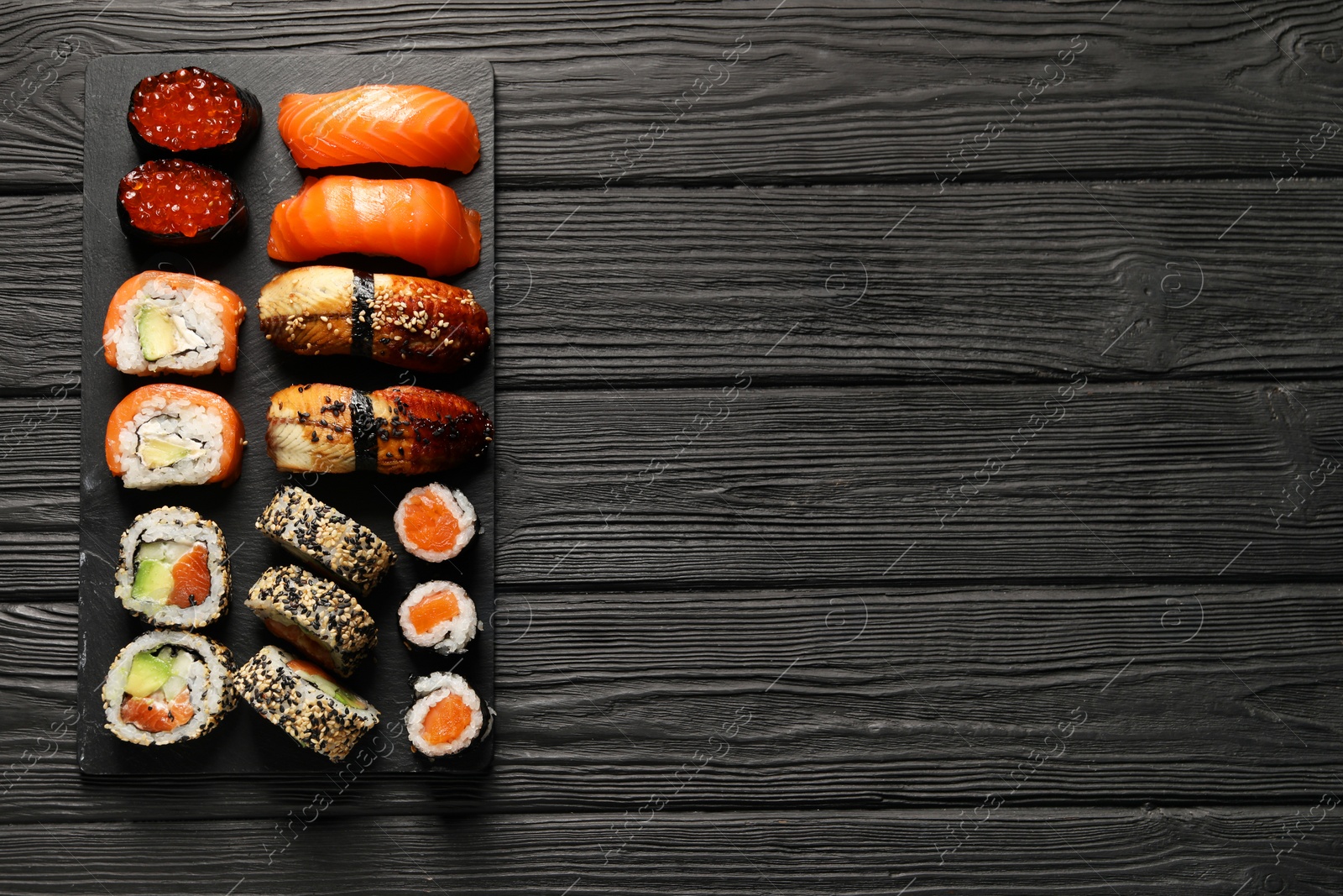 Photo of Set of delicious sushi rolls on black wooden table, top view. Space for text