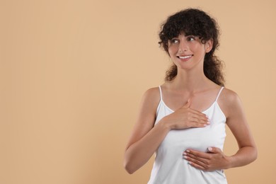 Photo of Smiling young woman doing breast self-examination on light brown background. Space for text