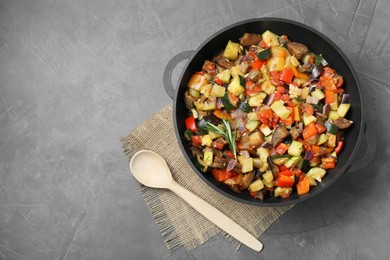 Photo of Delicious ratatouille in baking dish and wooden spoon on grey table, flat lay. Space for text