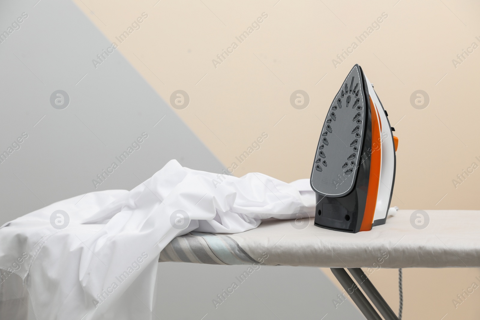 Photo of New modern iron and clean shirt on board against color background. Laundry day