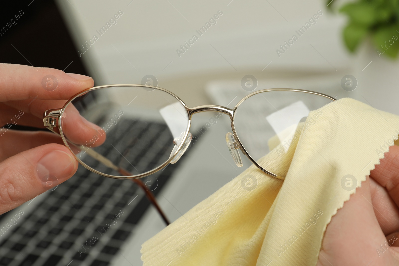 Photo of Woman cleaning glasses with microfiber cloth at home, closeup