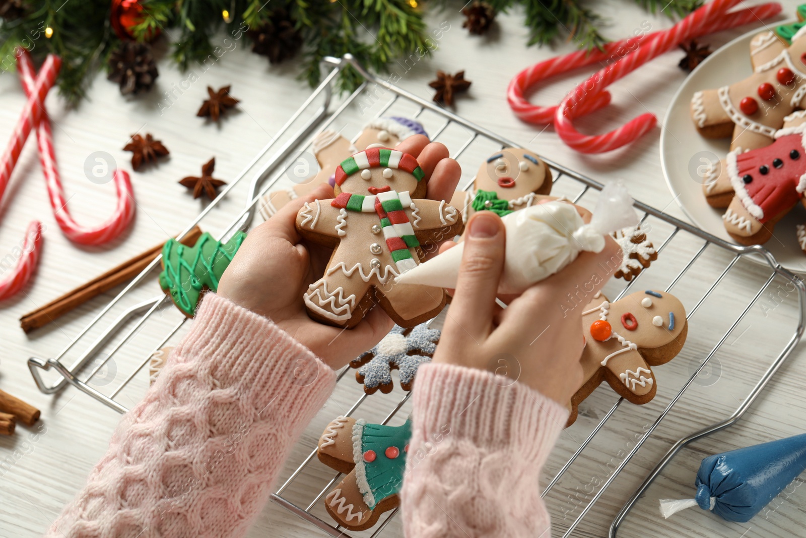 Photo of Making homemade Christmas cookies. Girl decorating gingerbread man at white wooden table, closeup