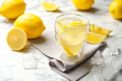 Glass with lemon water and ice cubes on marble table