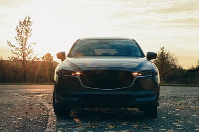 Photo of Black modern car parked on road at sunset