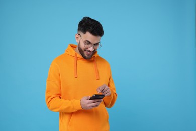 Photo of Happy young man using smartphone on light blue background, space for text