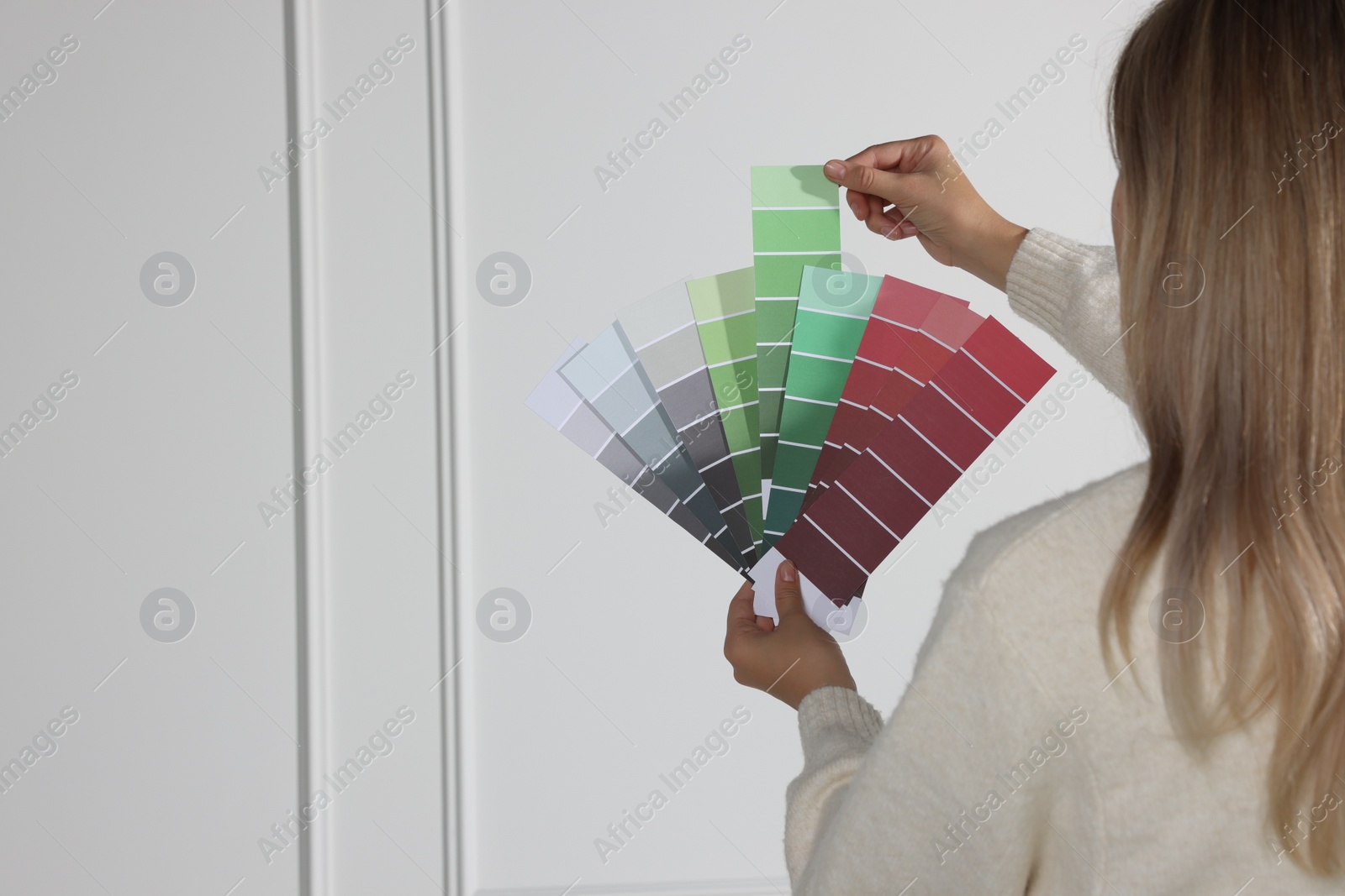 Photo of Woman choosing color for wall indoors, focus on hands with paint chips. Interior design