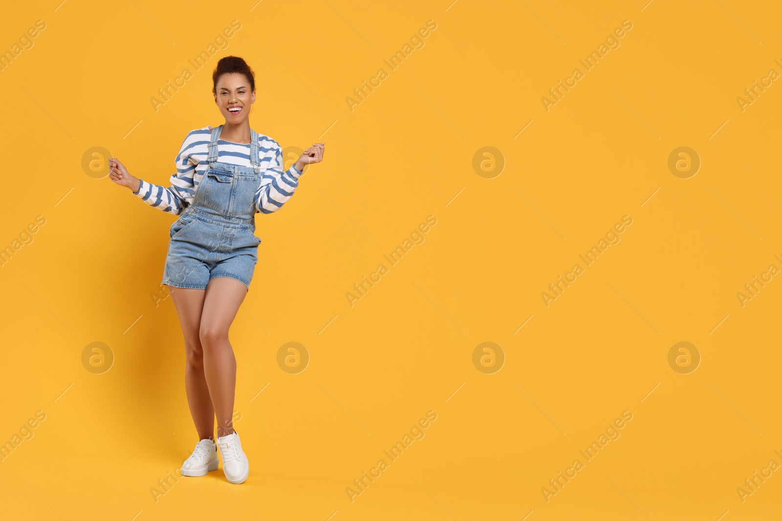 Photo of Happy young woman dancing on orange background. Space for text