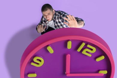 Deadline management. Man evading falling clock on violet background, above view